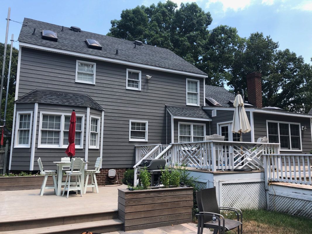 Gray two-story house with a wooden deck and backyard with trees, a table, and a red umbrella.