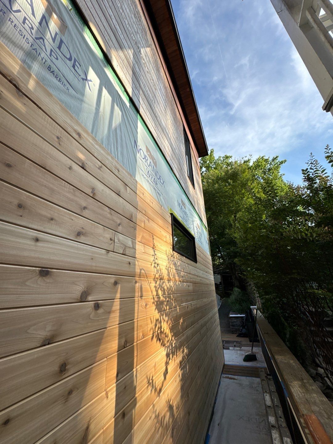 Building exterior with wood siding, partially covered in plastic wrap.
