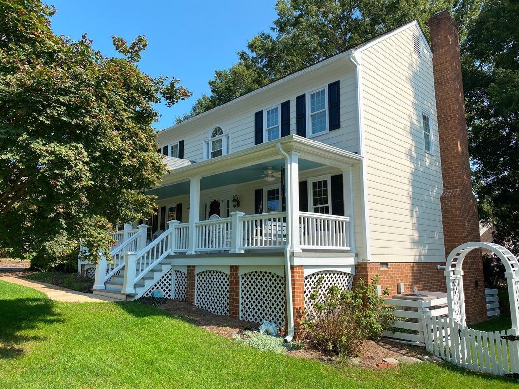 White two-story house with a porch and black shutters; red brick chimney; blue sky.