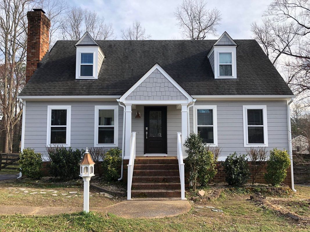Gray house with dark roof, dormers, and brick chimney. White trim and front steps, lawn.
