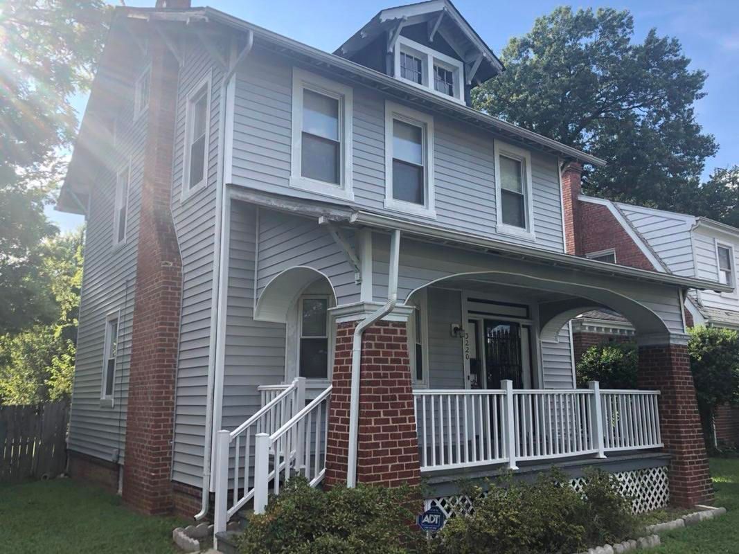 Two-story house with gray siding, red brick chimney, and a porch.