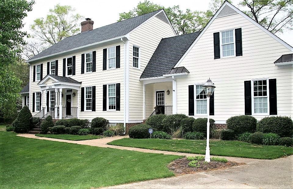 Two-story white house with black shutters, green lawn, and shrubbery.