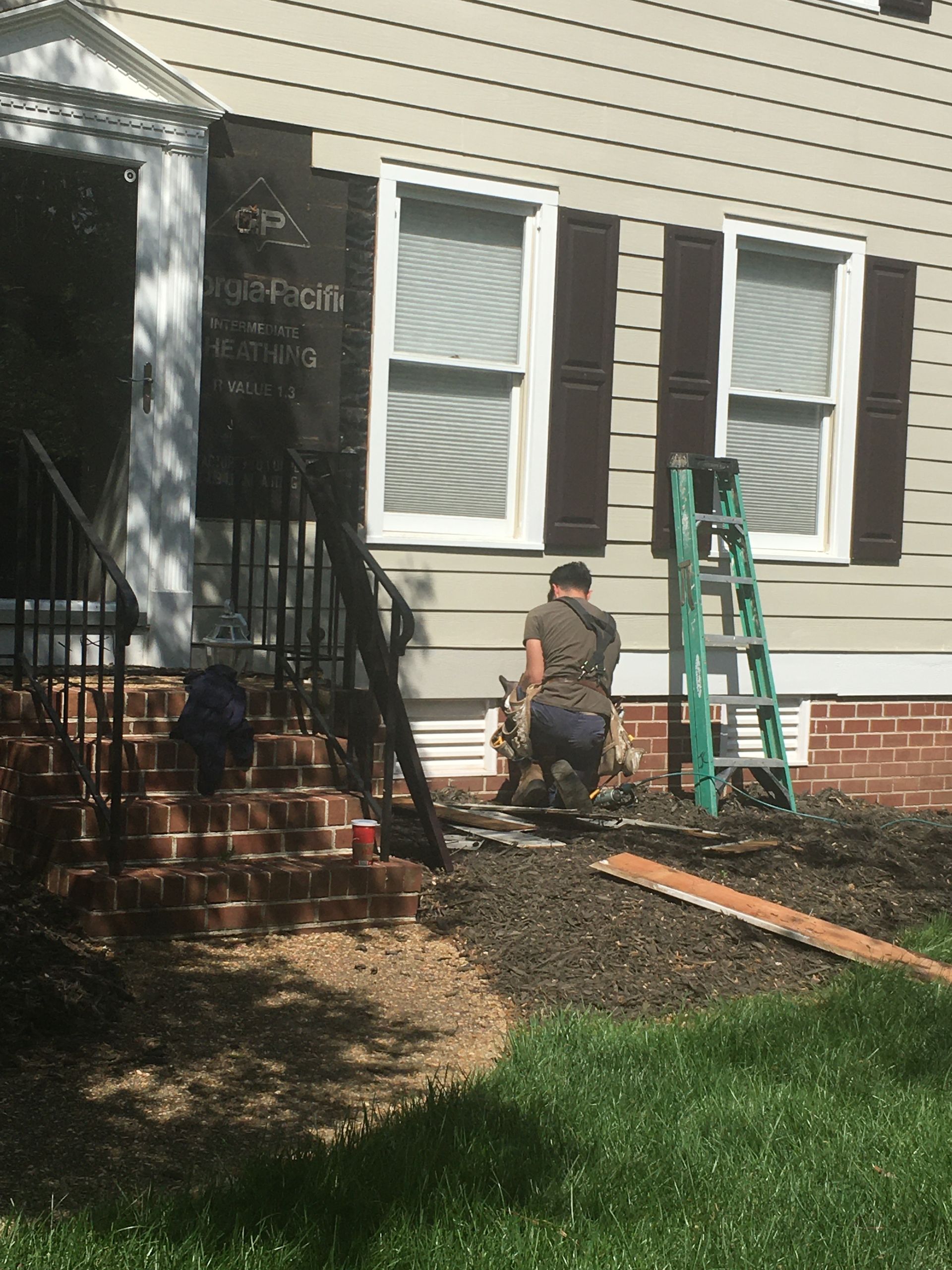 Person kneeling with dog in front of a house. A ladder leans against the building, and there are freshly planted flowers.