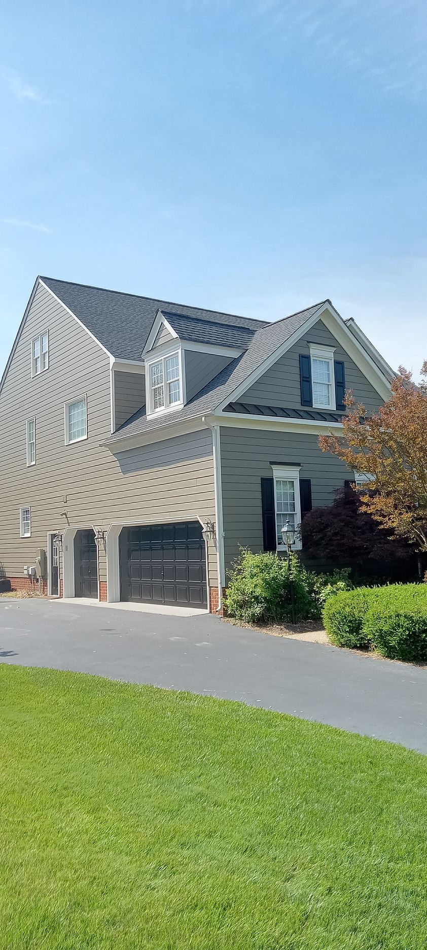A two-story gray house with a black driveway and green lawn under a blue sky.