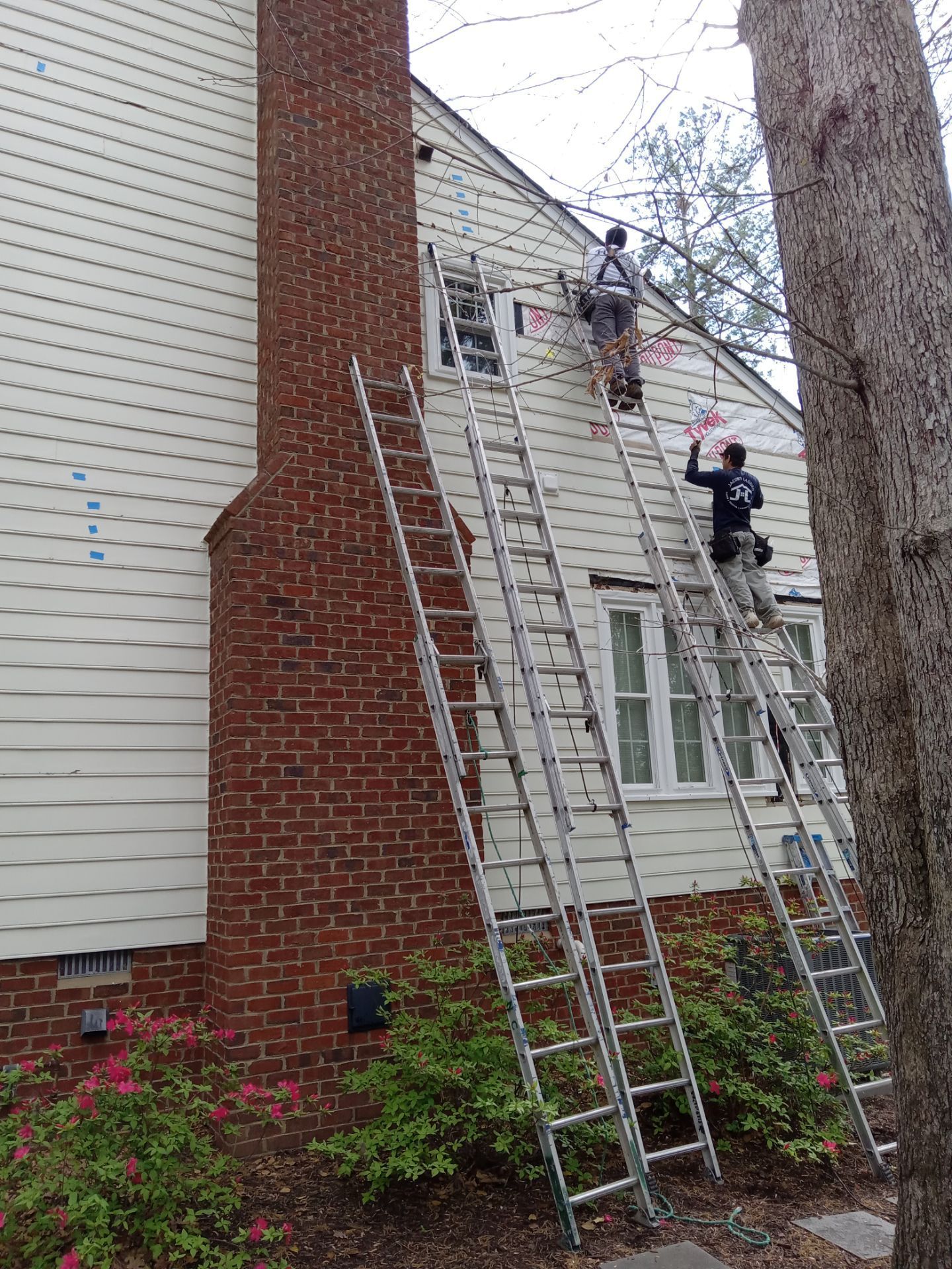 Three ladders leaning against a house with workers near windows, one by the chimney.