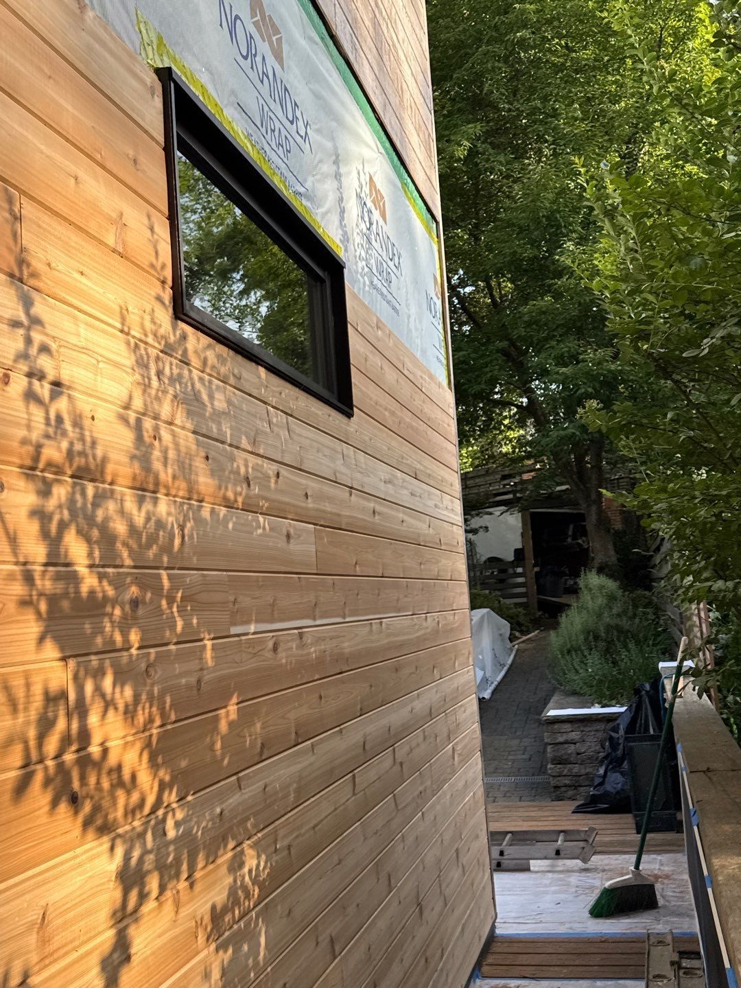 Side view of a building under construction with horizontal wood siding. A window is installed.