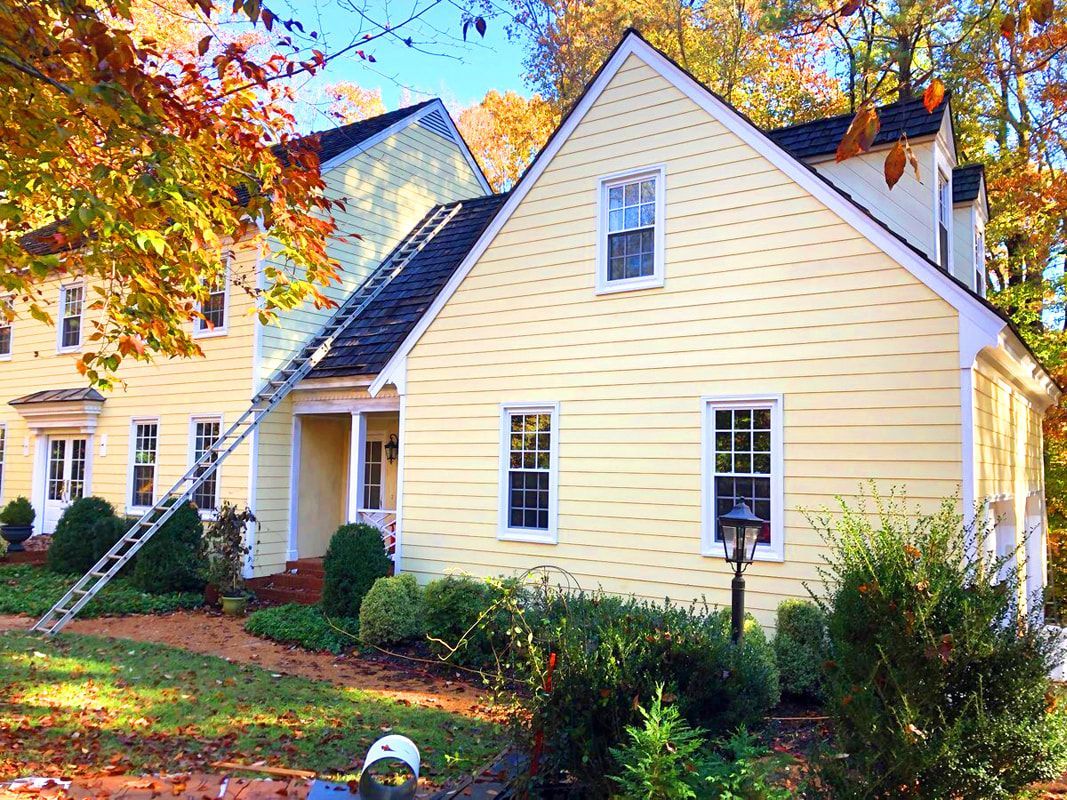 Yellow house with white trim, ladder against the roof, fall foliage.