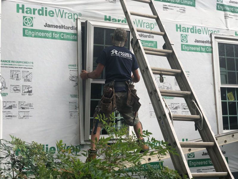Person installing a window, standing on ladder next to house with HardieWrap.