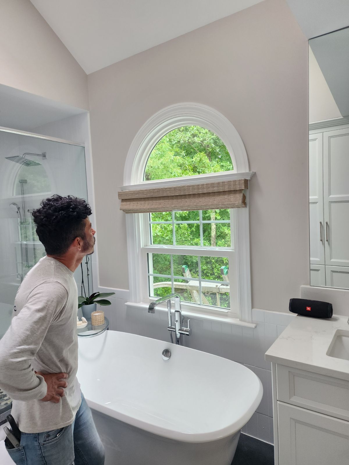 Person looking at a window in a bathroom with a tub. The window has a shade.
