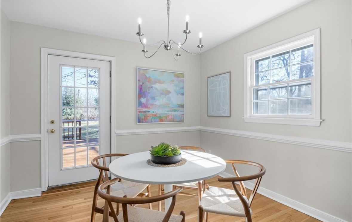Dining room with white table and chairs, chandelier, and a view of the outdoors.