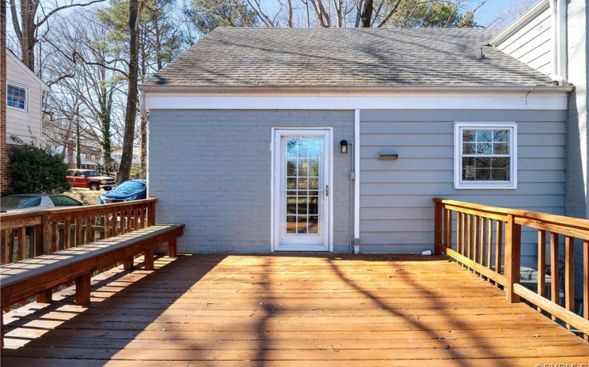 Wooden deck in front of a blue-gray house with a white door and window. Sunny day.