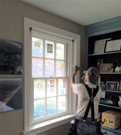 Person caulking a white window frame indoors, near a bookshelf.