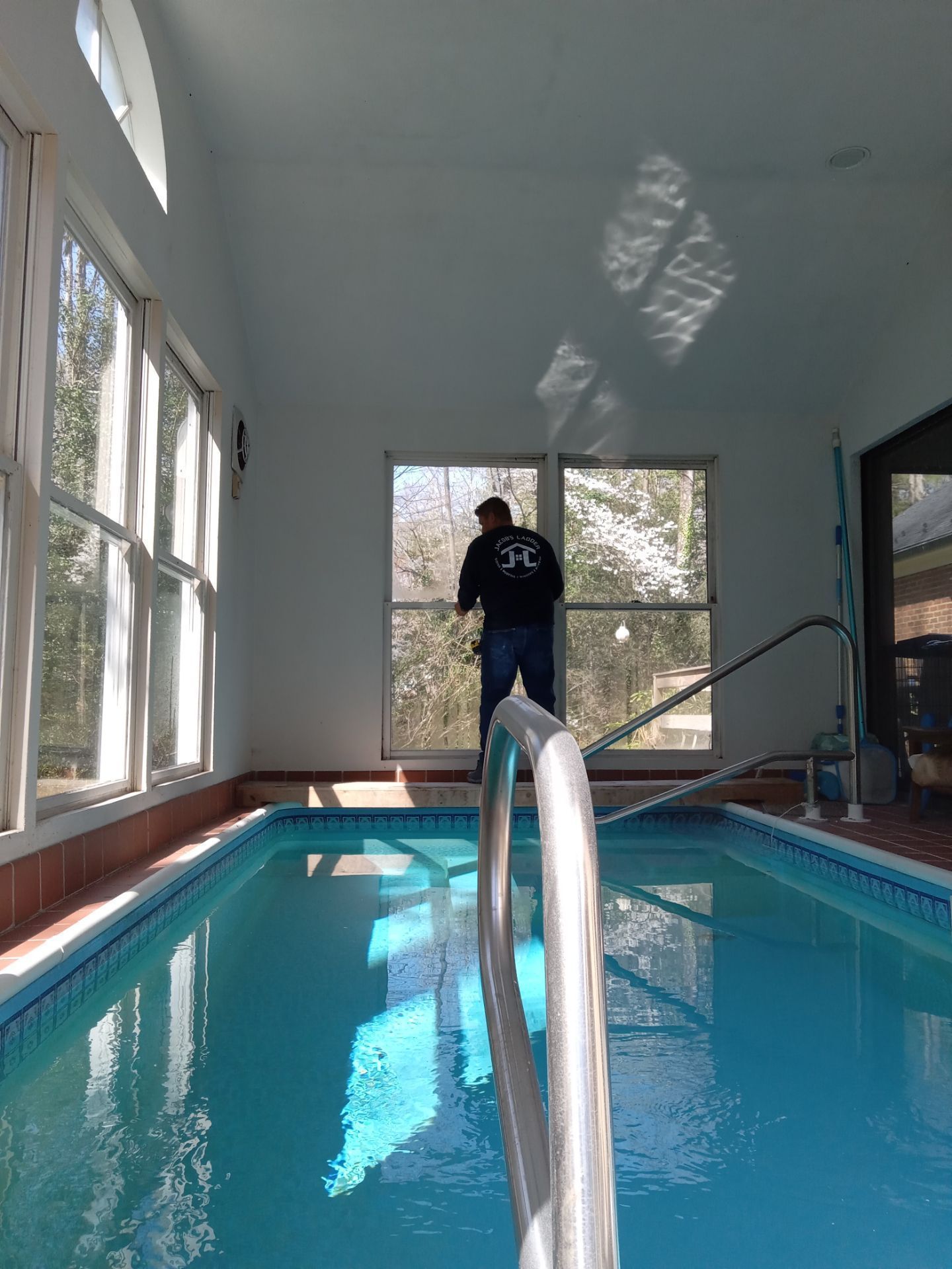 Indoor swimming pool with person looking out a window. Sunlight streams through windows, reflecting on the water.