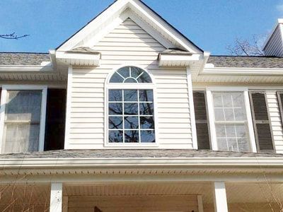 White house exterior with arched window, shutters, and siding.