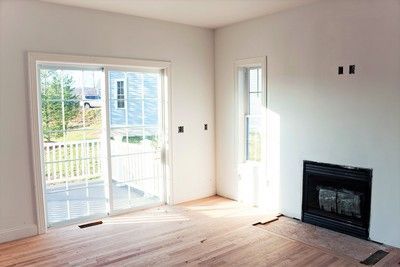 Empty room with a fireplace, sliding glass door, and window. Bare wood floor.