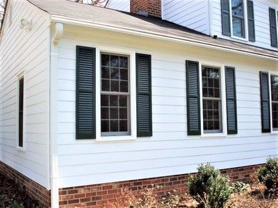 White house exterior with dark green shutters, brick foundation, and small bushes.