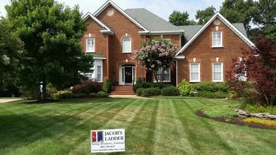 Brick house with green lawn, trees, and landscaping, with a 