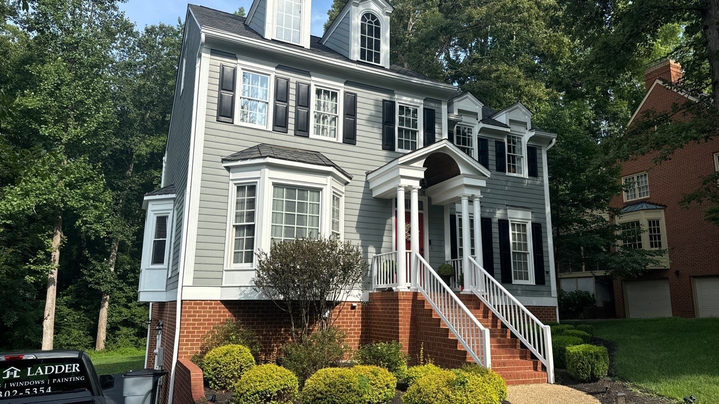 Gray multi-story house with brick foundation, black shutters, and white trim.