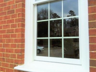 White-framed window on a red brick building, reflecting trees, a car, and other buildings.
