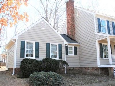 Beige house with a red brick chimney, green shutters, and a small porch.