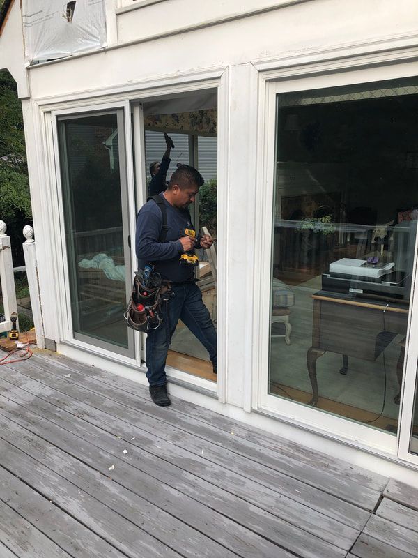 Man working on a sliding glass door on an outdoor deck, using a drill.