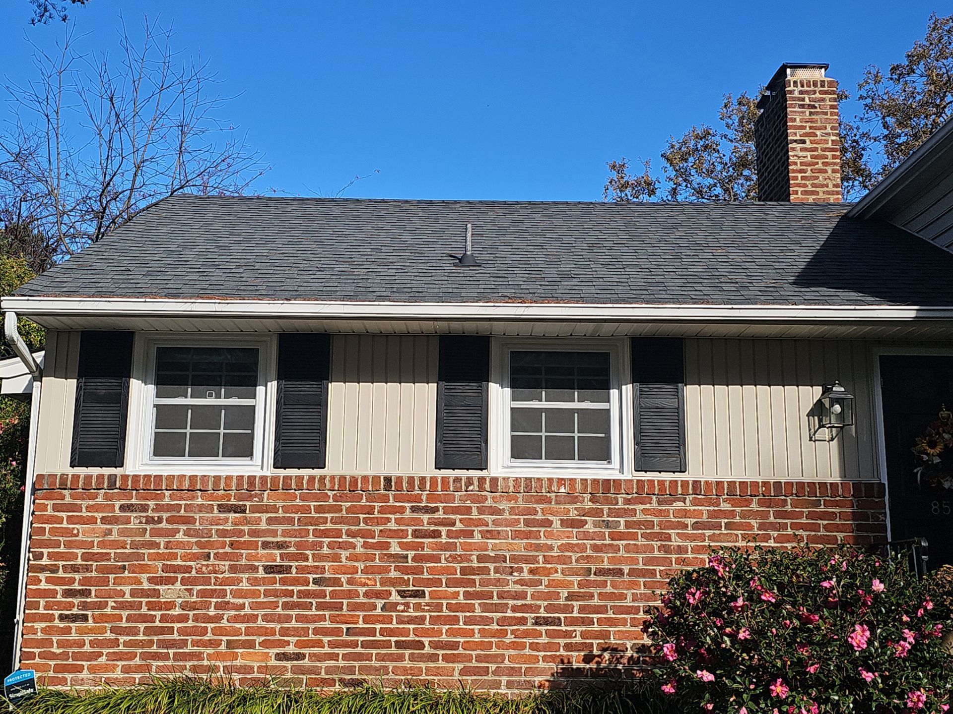 Residential house with brick base, cream siding, two windows with shutters, and dark gray roof.