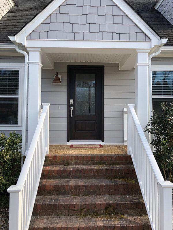 A gray house front with white railings, brick steps, and a dark front door under a small portico.
