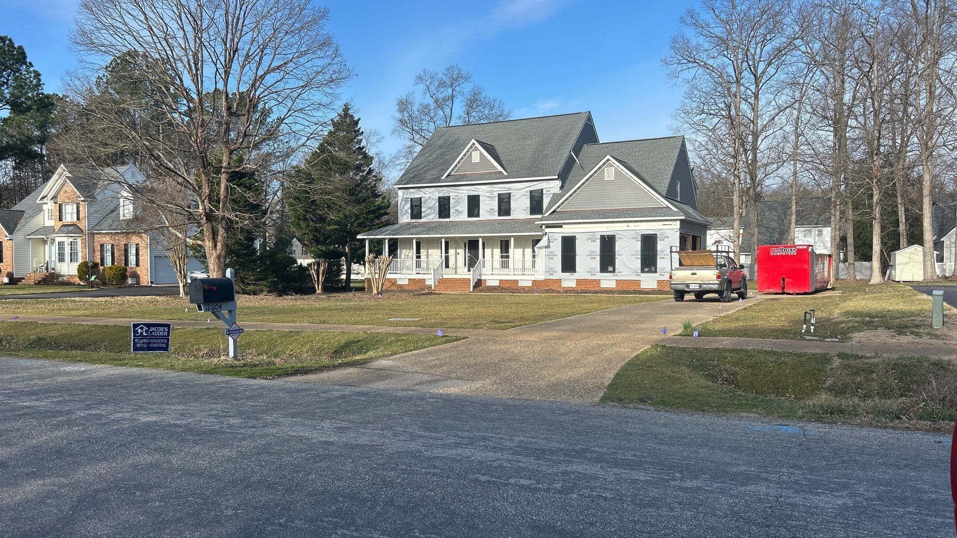 A two-story house with a porch and a smaller house next door on a sunny day.