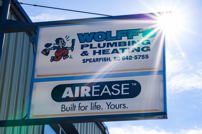 Sign for Wolff's Plumbing & Heating in Spearfish, SD, also advertising Airease. Bright sun.