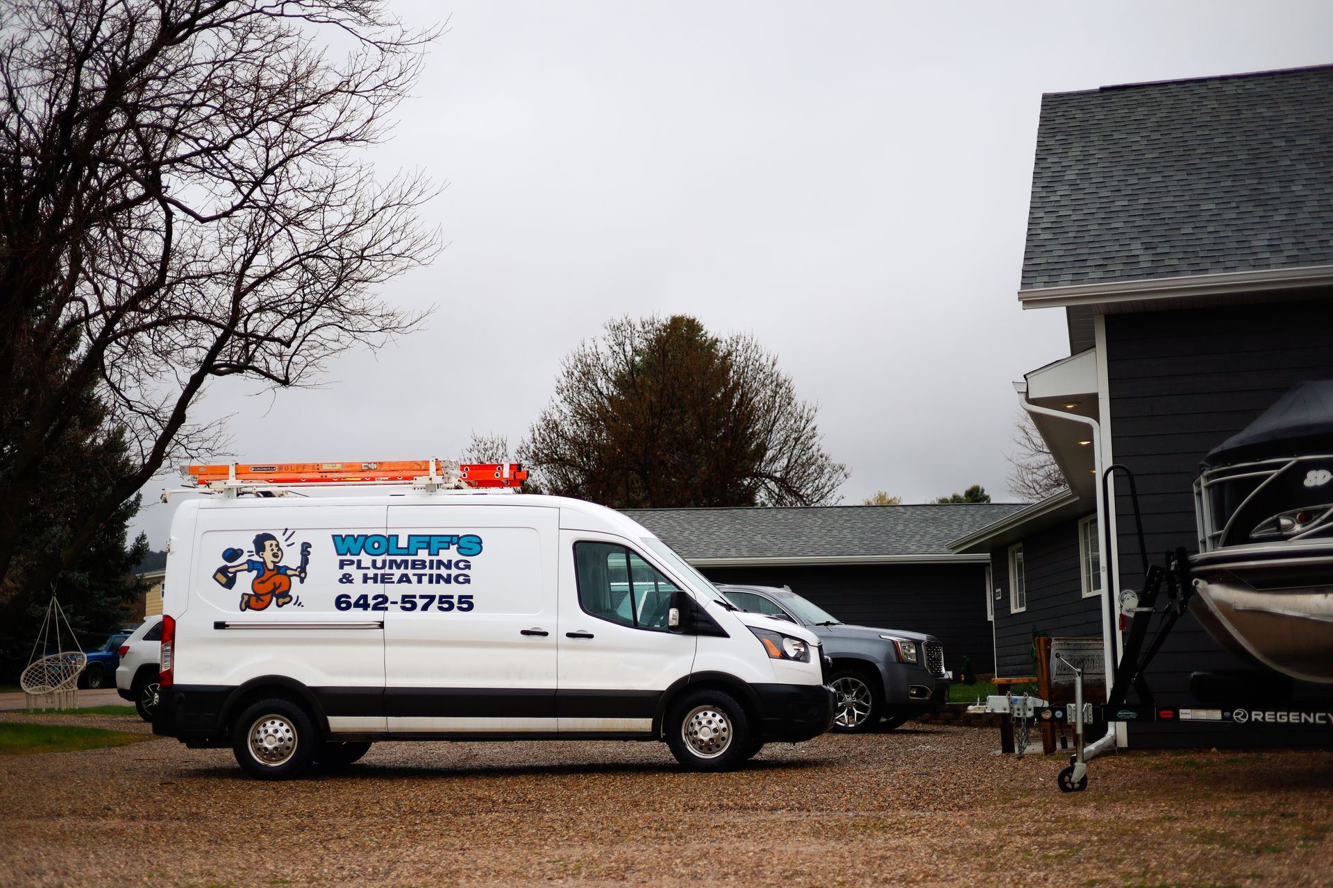 White work van parked in a gravel driveway, logo on the side, next to a house and a boat.
