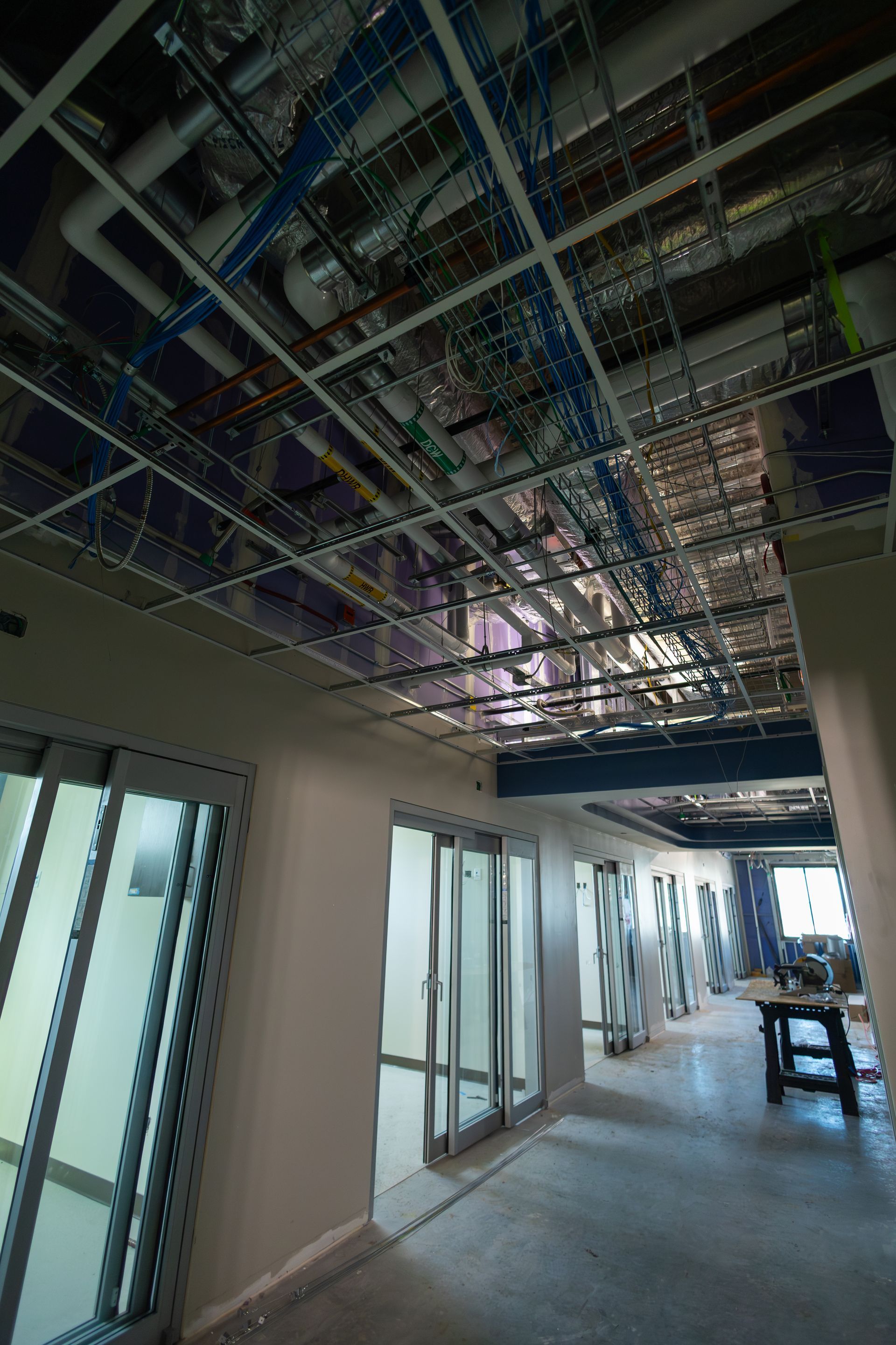 Interior hallway construction with exposed ceiling infrastructure; glass doors.