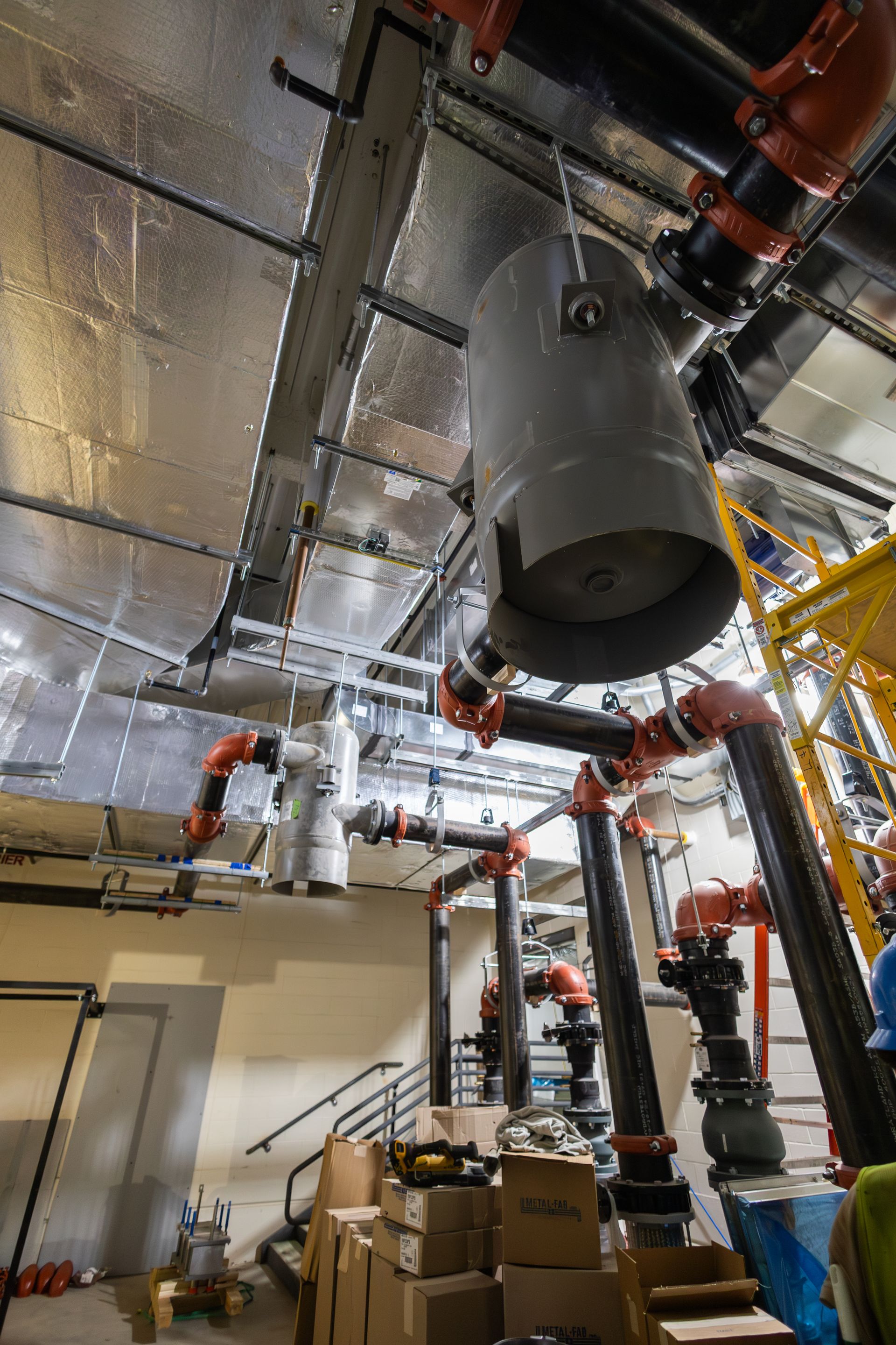 Industrial interior with pipes, a large gray tank, and boxes; ceiling with silver insulation.