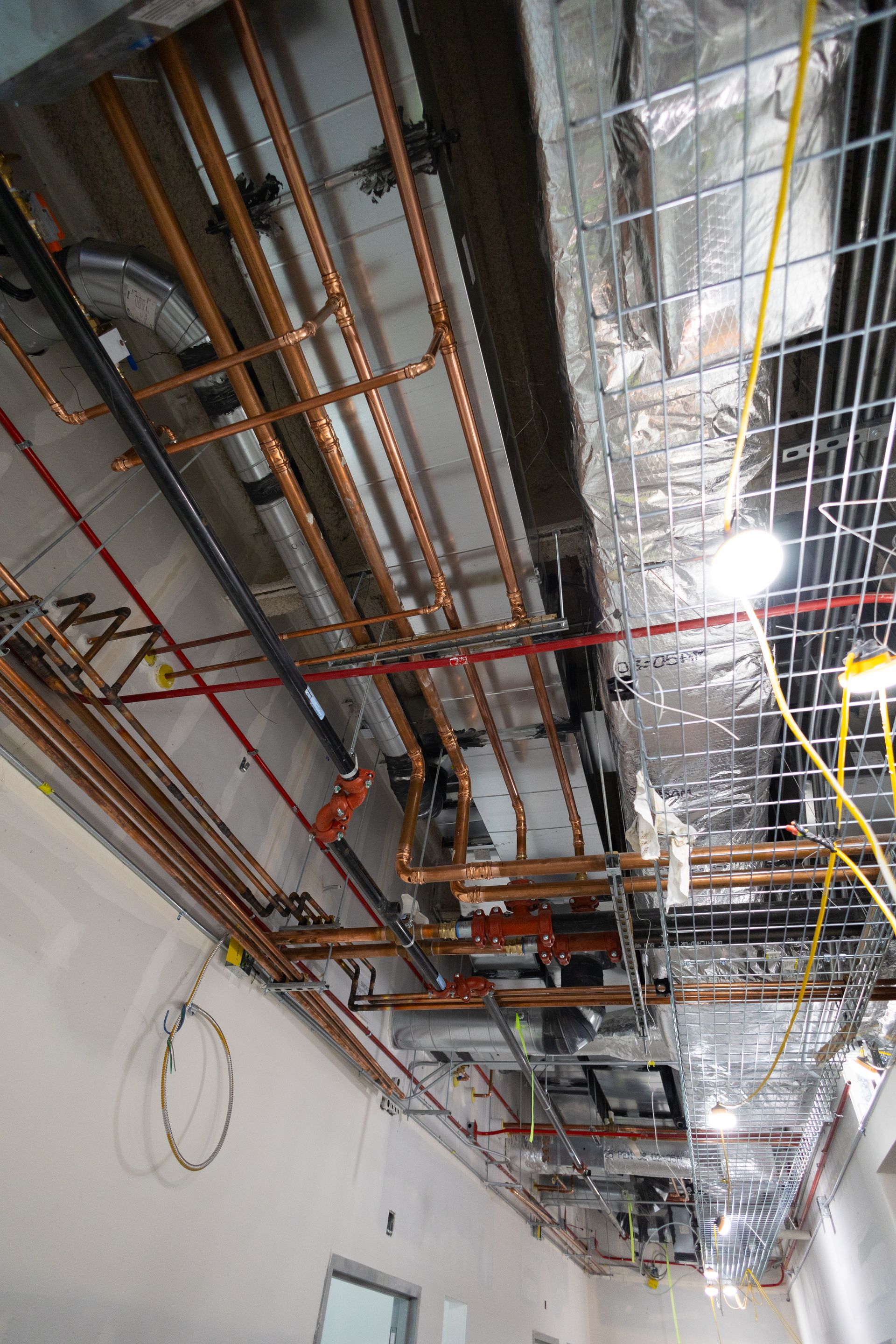 Overhead view of unfinished ceiling with copper pipes, ductwork, and electrical wiring.