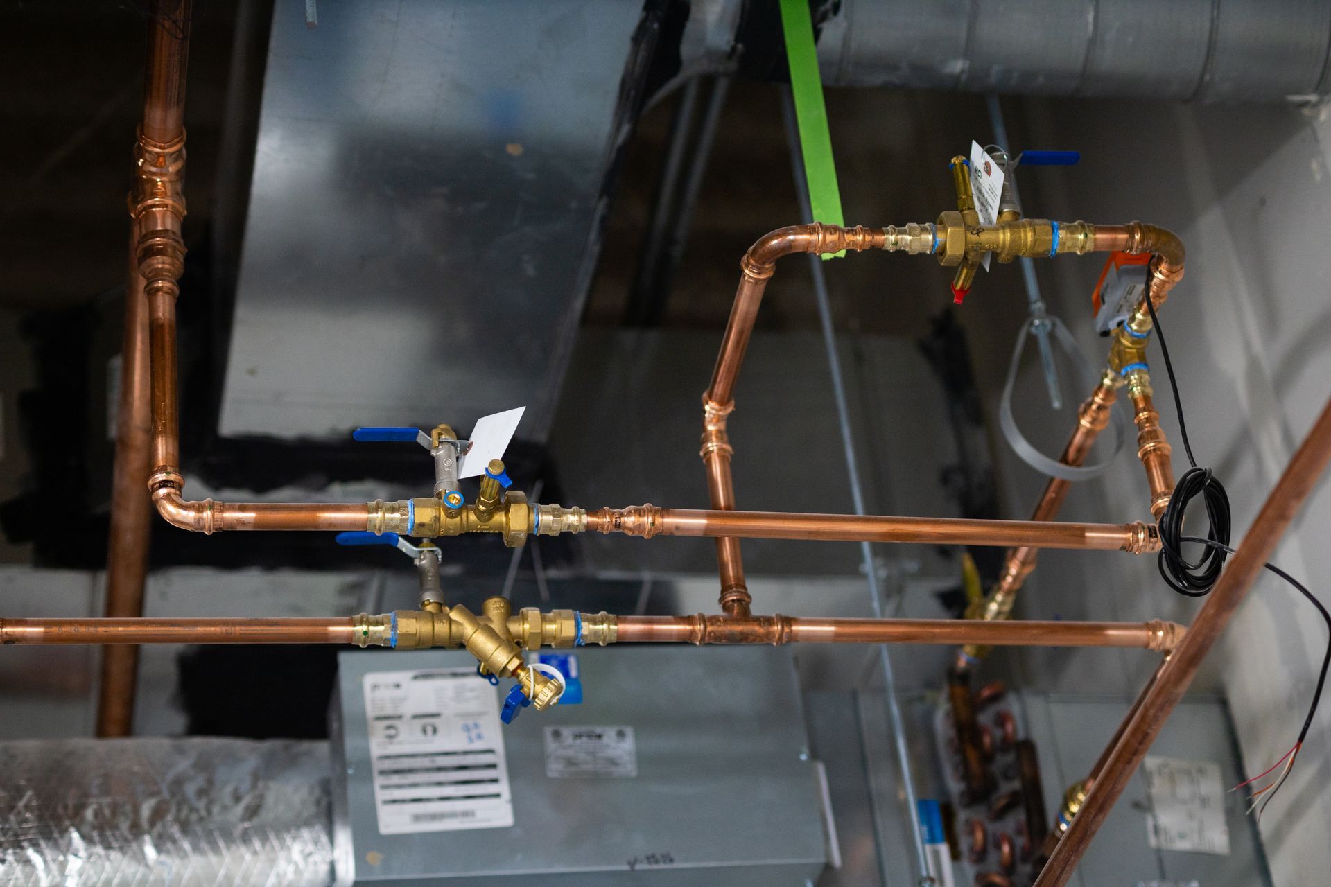 Copper pipes with valves installed near HVAC ductwork.