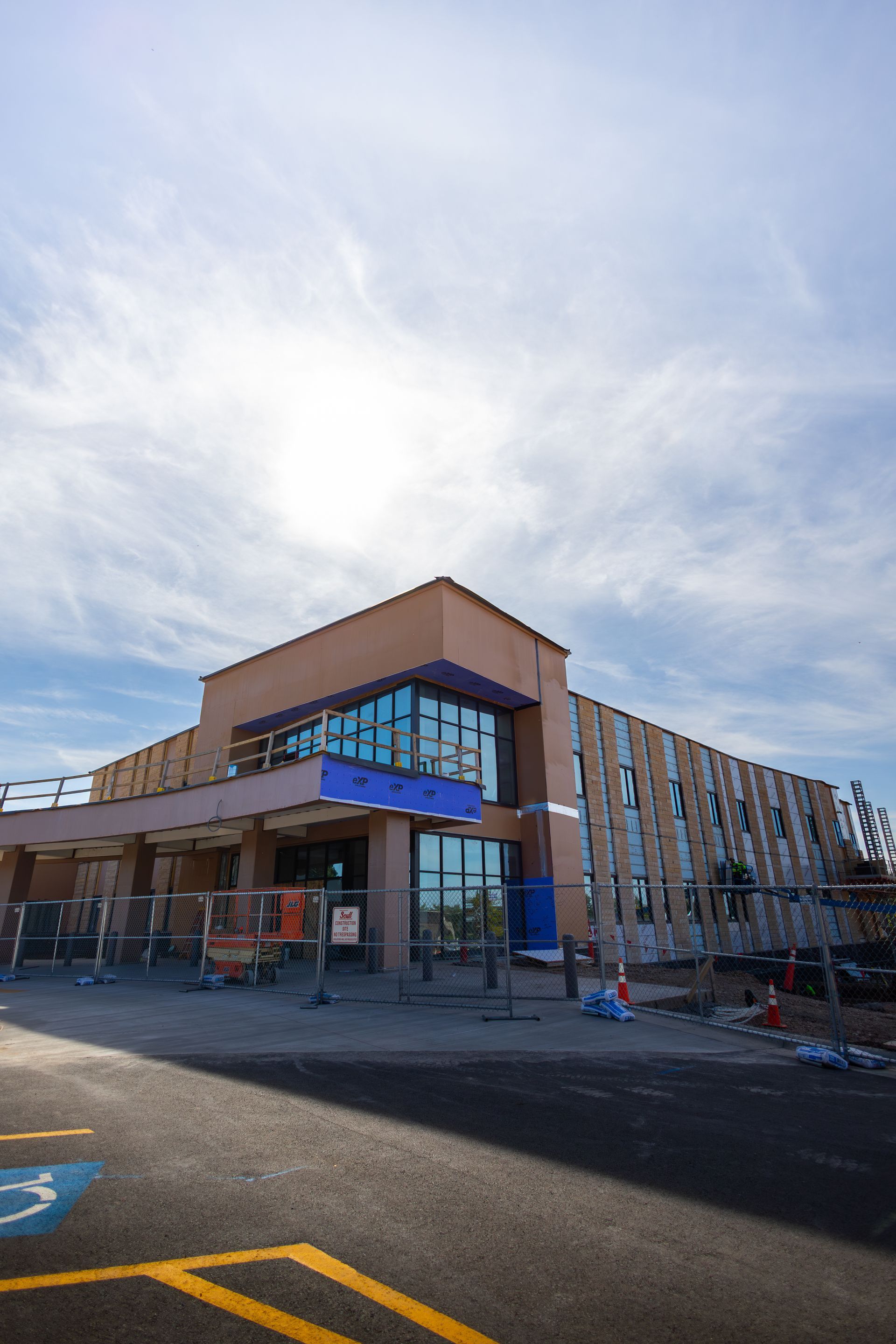 Building under construction, brown facade, blue accents, clear sky, parking lot with a handicap parking symbol.
