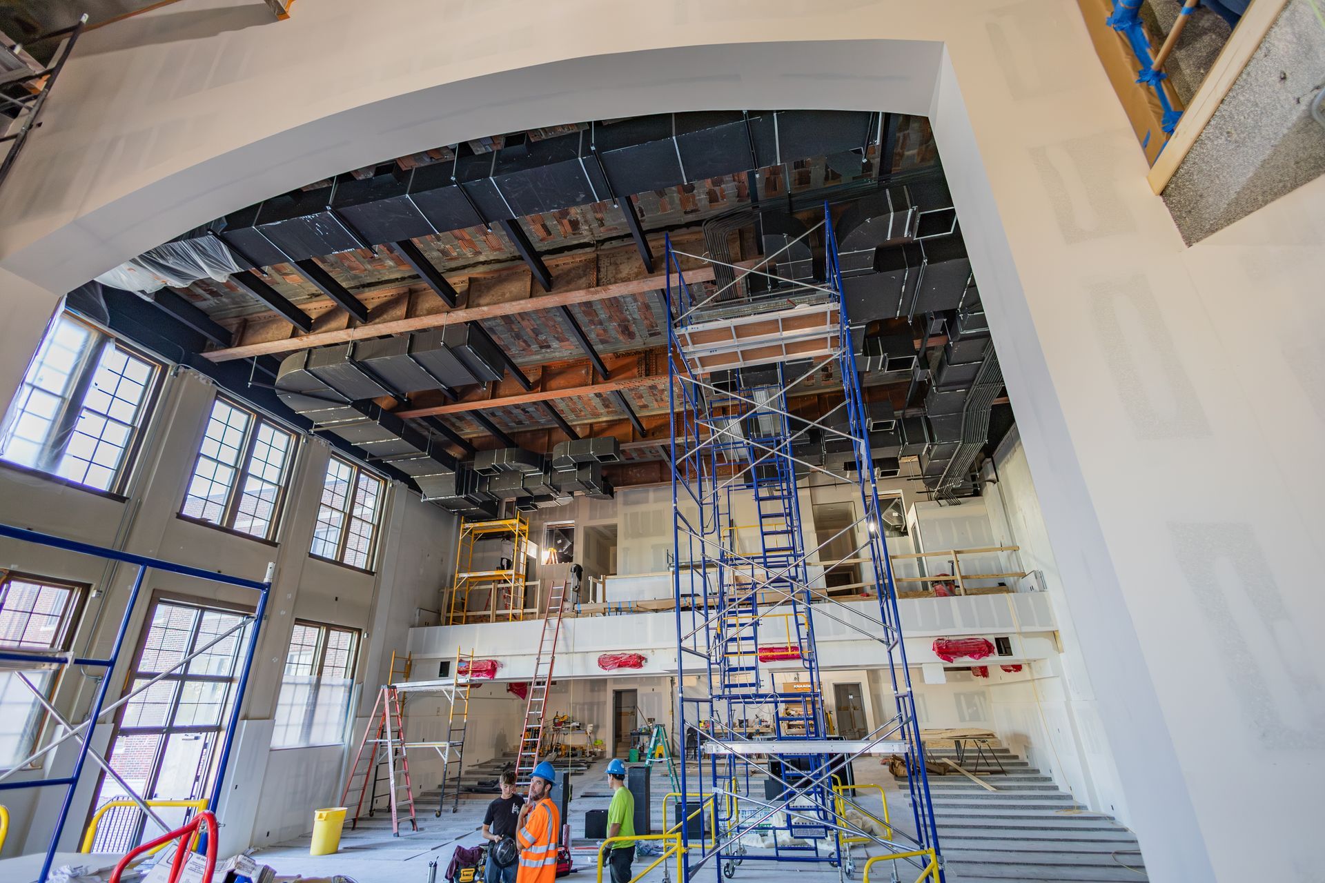 Interior of a building under construction, scaffolding, exposed ceiling, arched doorway, and workers.