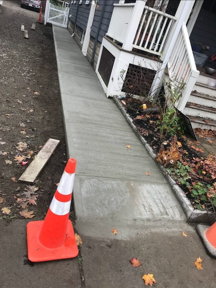 An orange and white traffic cone is sitting on the sidewalk next to a concrete walkway.