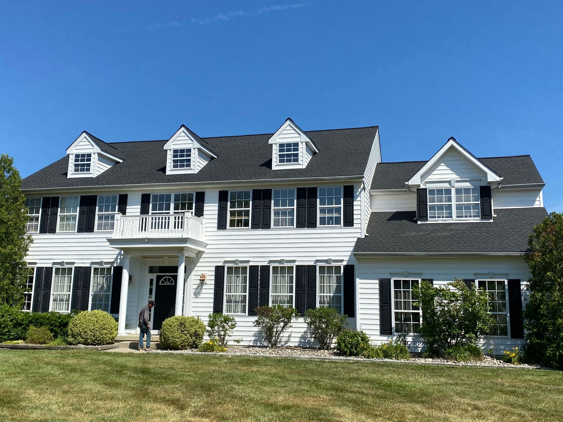 Two-story white house with black shutters and roof against a blue sky.