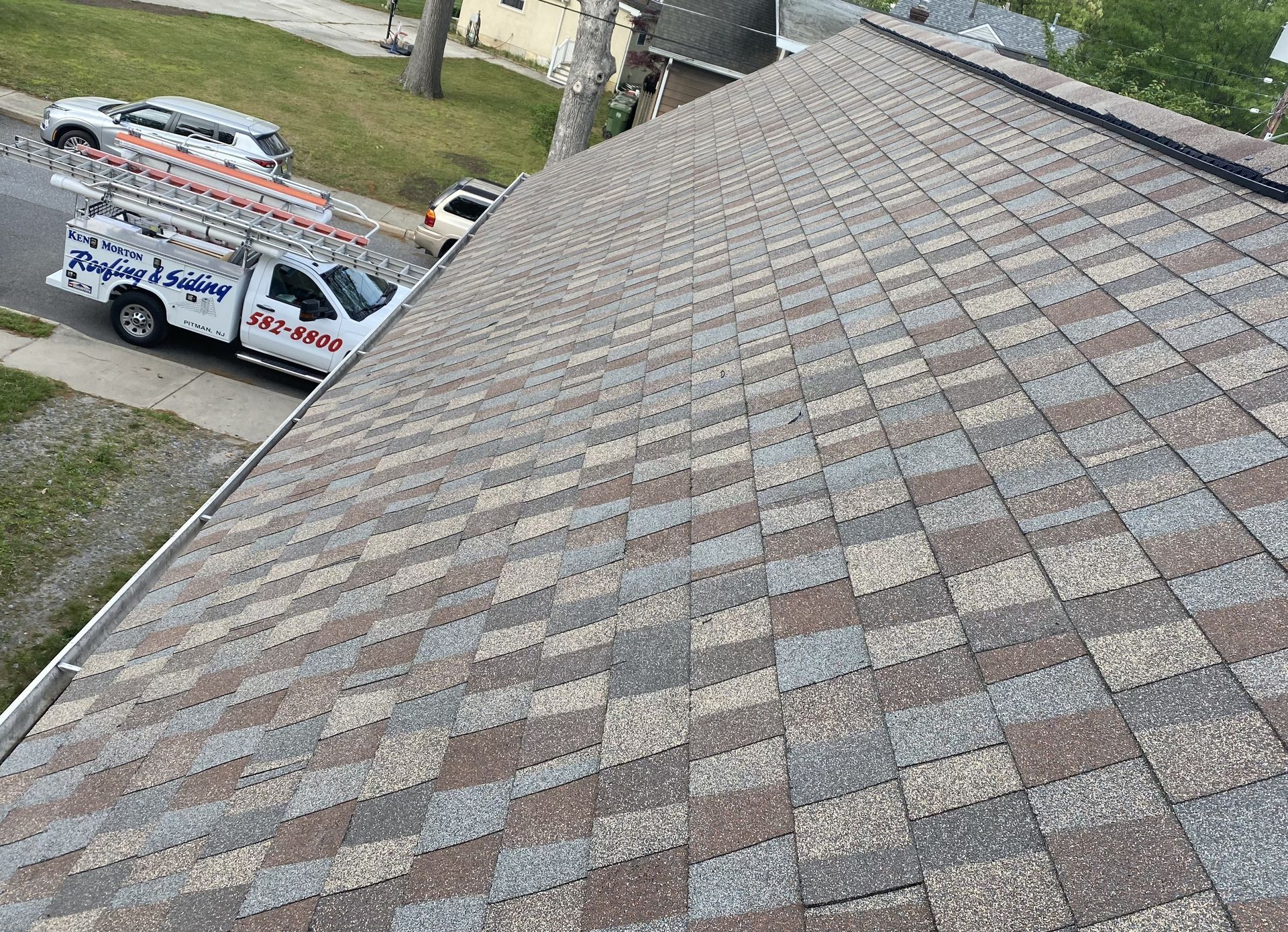 New asphalt shingle roof in shades of brown and grey; a white work truck is parked nearby.