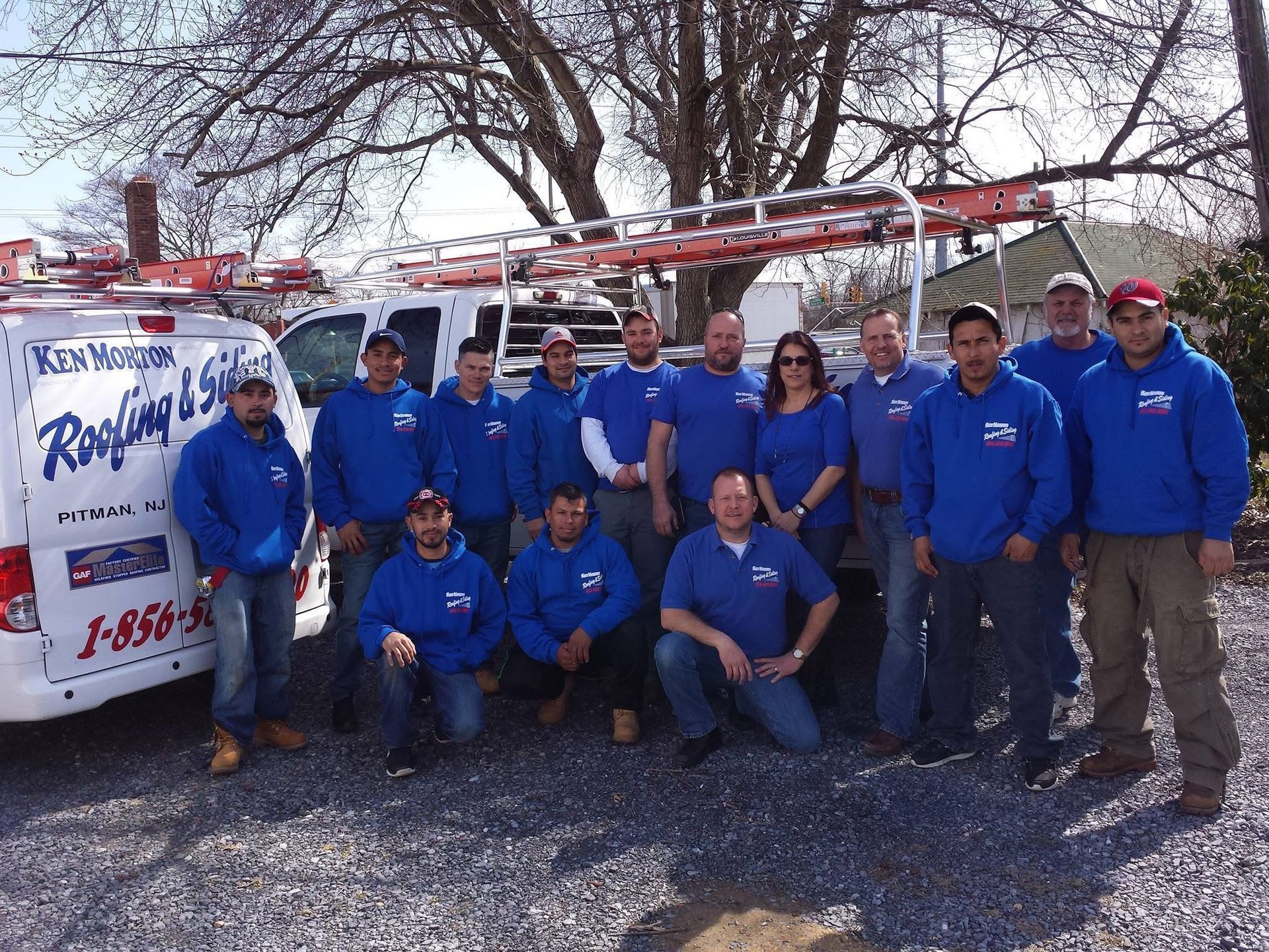 Group of roofers in blue hoodies pose with a van that reads 