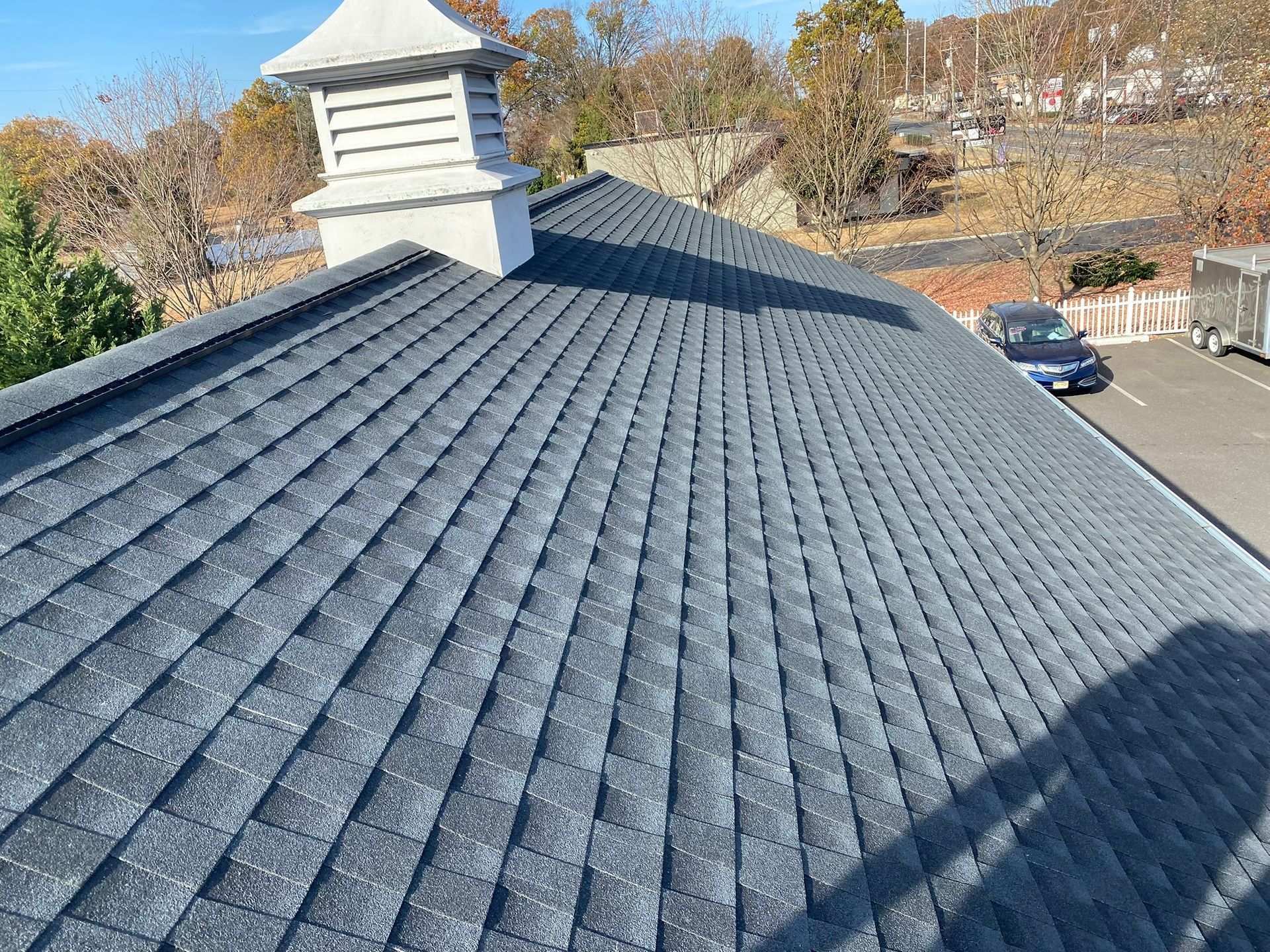A blue shingled roof with a white cupola. Sunlight casts a shadow on the roof.