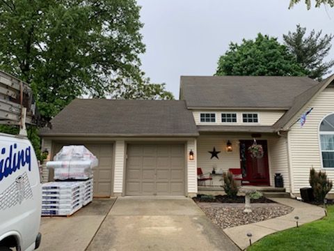 House with new roof, garage, and van loaded with roofing materials. Overcast day.