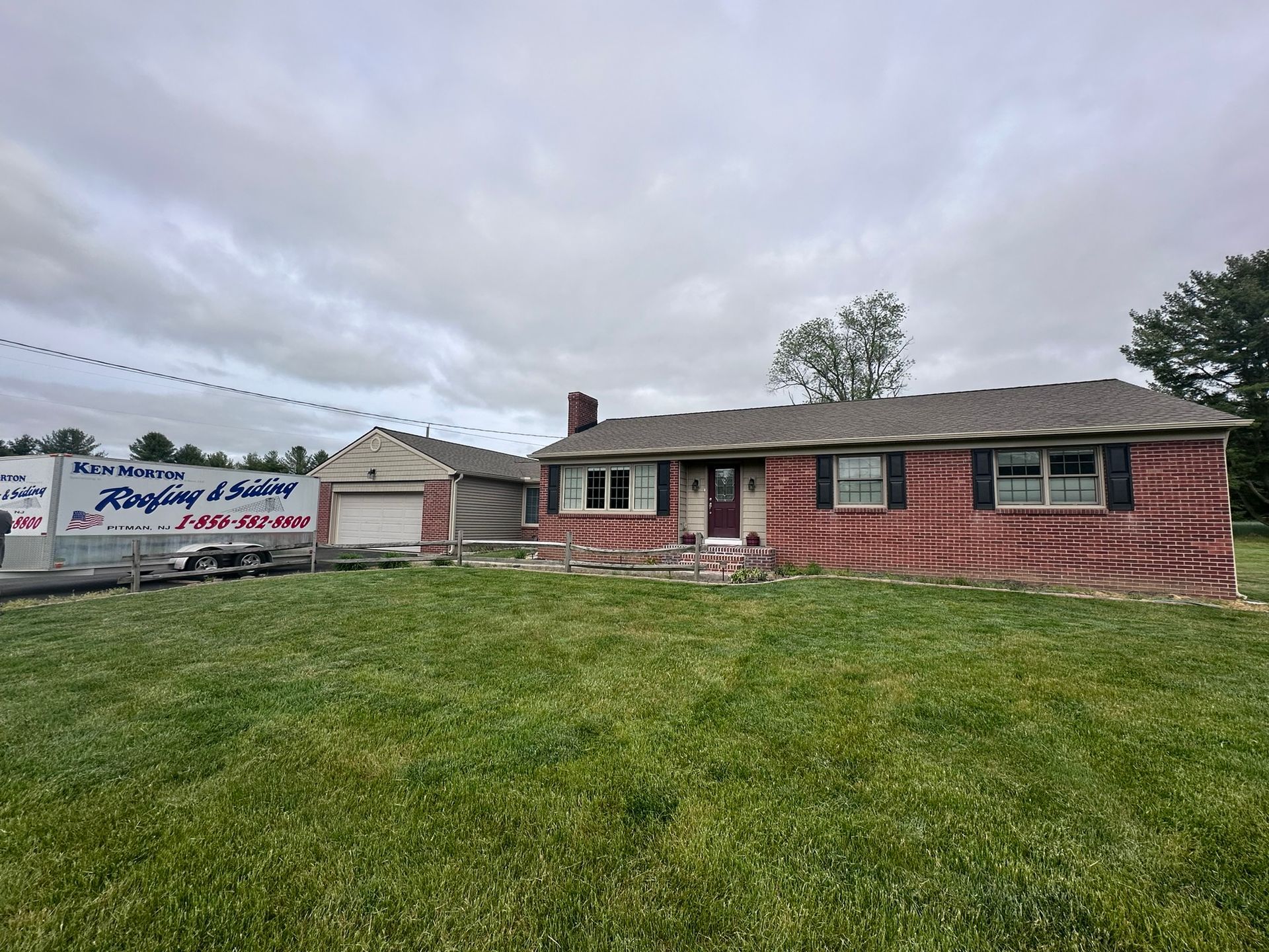 Red brick house with a garage, a green lawn, and a cloudy sky.