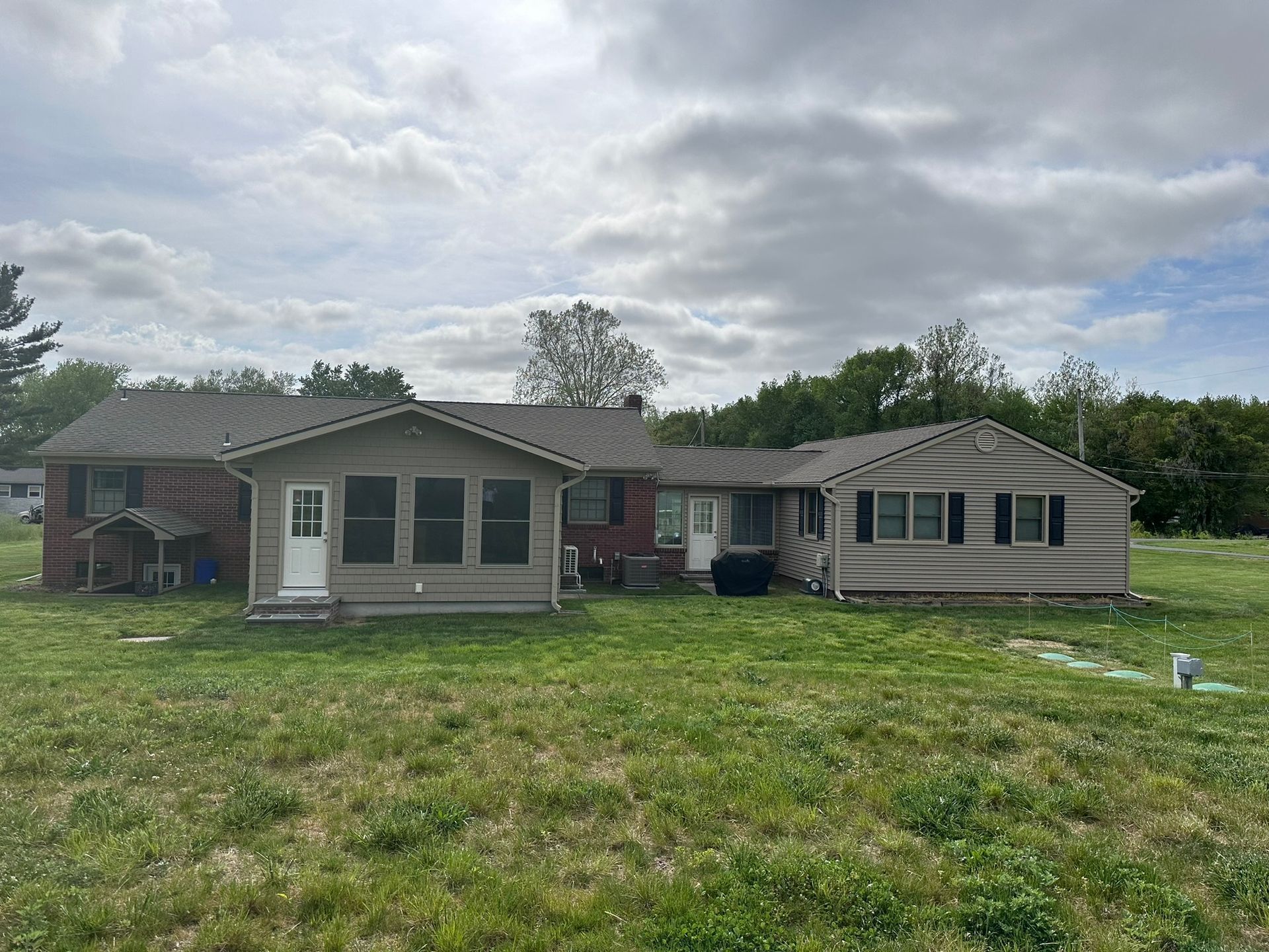 A ranch-style house with three sections of varying colors, surrounded by a grassy yard under a cloudy sky.
