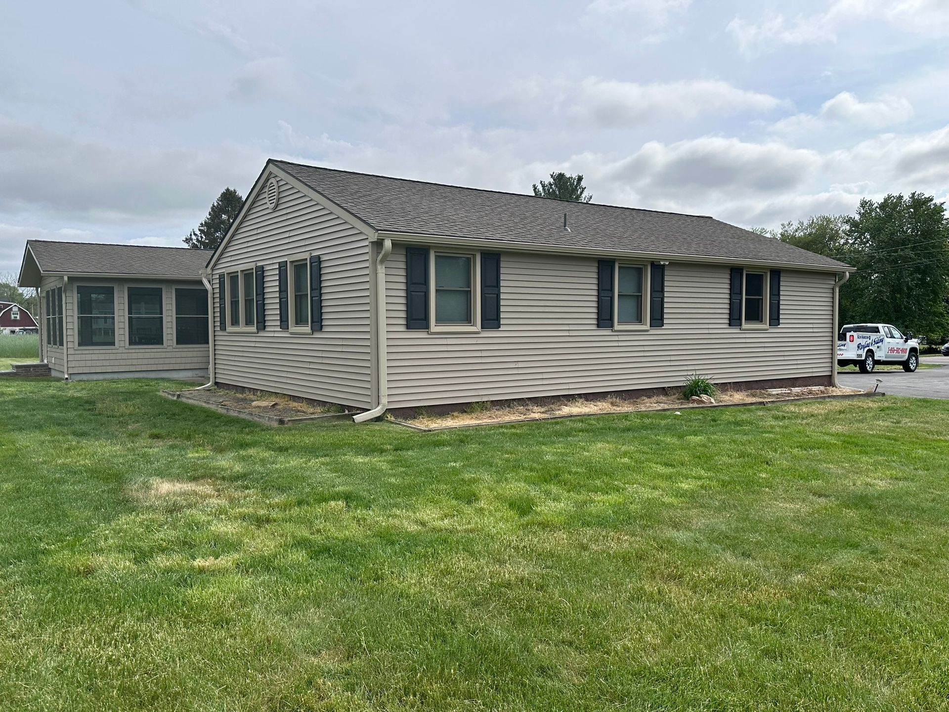 Tan one-story building with black shutters and a green lawn. A white truck is parked nearby.