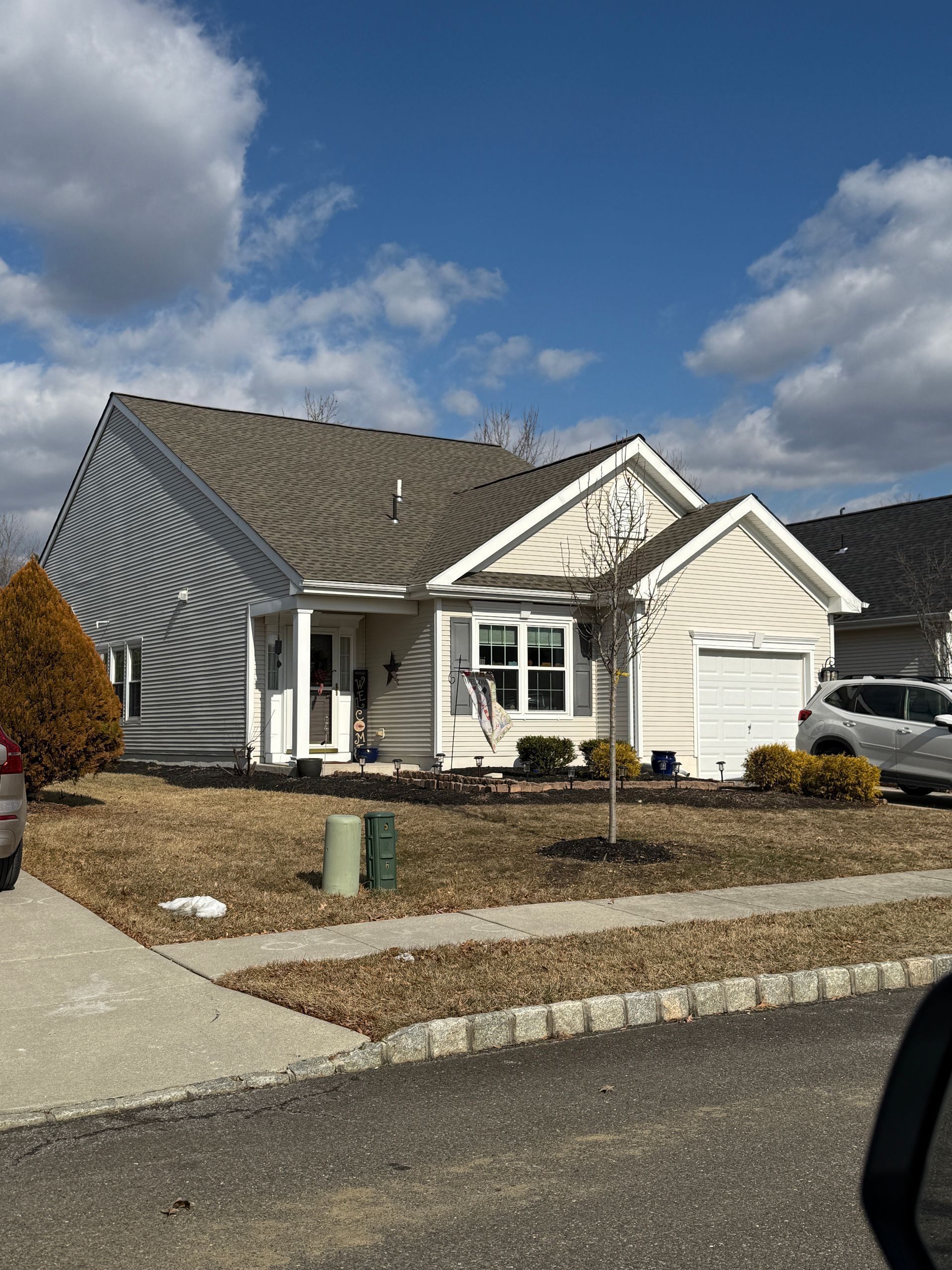 Tan house with brown roof and garage on a sunny day. Dry grass in yard.