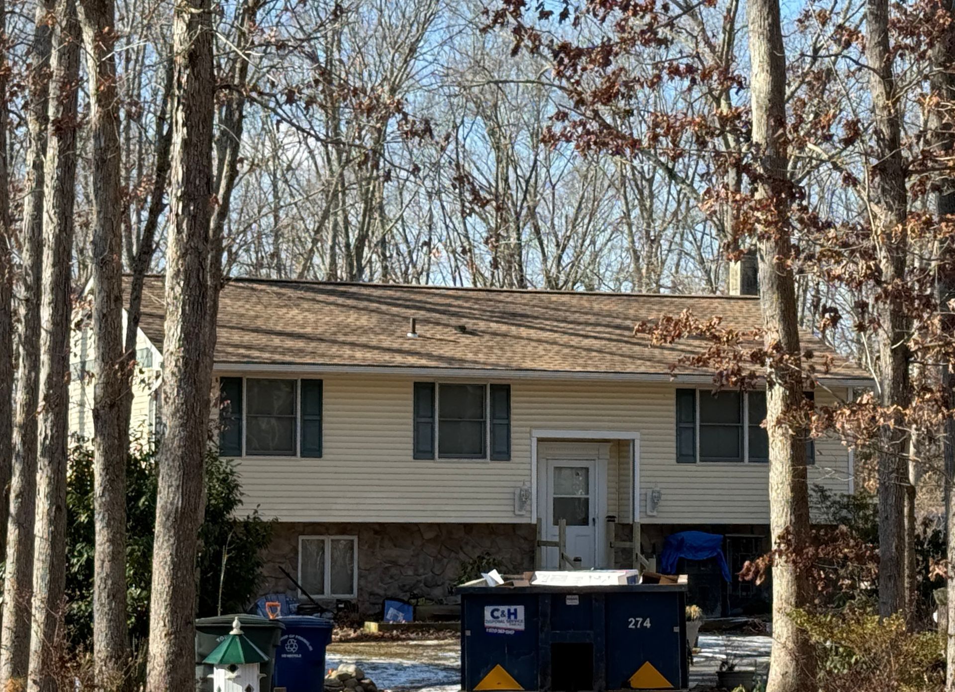 A light-colored house with a brown roof and visible trees in front of it.
