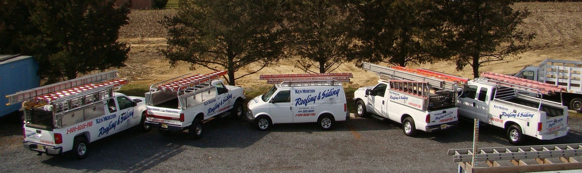 Multiple white service trucks with ladders parked outside. The trucks have business logos on the sides.