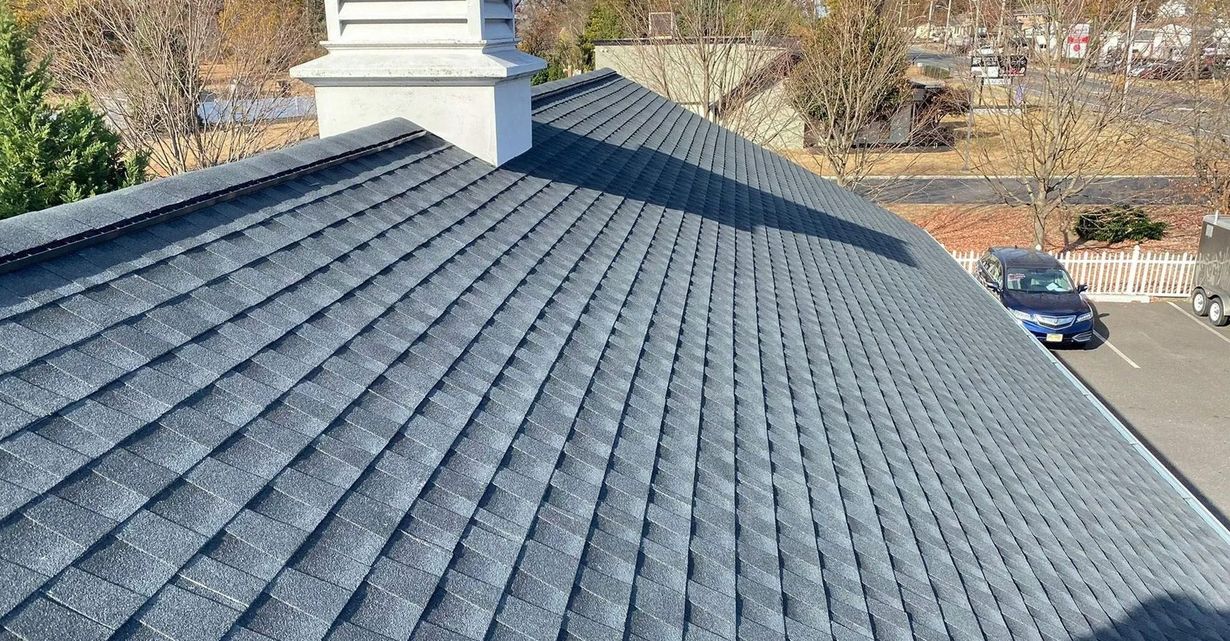 Dark gray asphalt shingle roof with a white chimney in an outdoor setting.