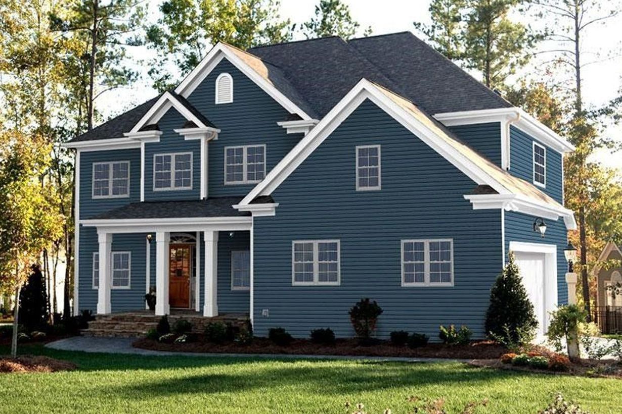 Two-story house with blue siding, white trim, dark roof, and brown front door. Green grass and trees surround.